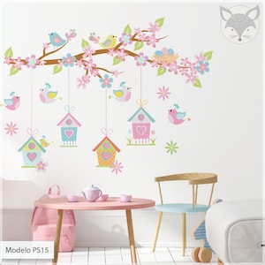 May include: A pink and brown birdhouse wall decal with a branch, flowers, and birds. The decal is on a white wall with a pink table and chair in the foreground. The text "Modelo PS15" is at the bottom of the image.
