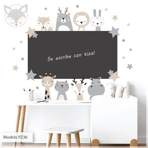 Puede incluir: Una pizarra negra con marco blanco y fondo blanco. La pizarra tiene un borde blanco y el texto "Se escribe con tiza!" escrito en negro. Hay varias pegatinas de animales en la pizarra, incluyendo un zorro, un ciervo, un león, un conejo, una jirafa, un gato y un hipopótamo. También hay varias estrellas blancas en el fondo.
