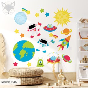 Puede incluir: Una pared blanca con una variedad de pegatinas coloridas con temática espacial, incluyendo astronautas, planetas, estrellas, cohetes y OVNIs. Las pegatinas están dispuestas en un patrón caprichoso, creando un ambiente divertido y alegre. El texto "Modelo PC02" es visible en la parte inferior de la imagen.