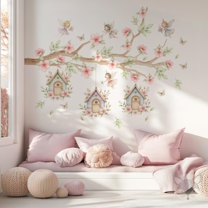 Puede incluir: Un vinilo decorativo de pared con una rama de árbol con flores rosas, hadas y casitas. La escena incluye mariposas y está situada sobre un banco acolchado rosa con cojines y pufs de punto, creando un espacio de cuento de hadas.