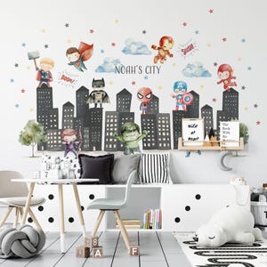 Peut inclure: Une décoration murale fantaisiste représentant des super-héros au-dessus d'un paysage urbain. La conception comprend des illustrations de Thor, Superman, Batman, Spider-Man, Captain America, et d'autres. Les mots "NOAH'S CITY" sont également inclus.
