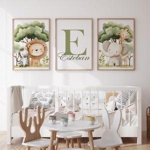 Puede incluir: Tres cuadros de pared con ilustraciones en acuarela. El cuadro de la izquierda muestra una cebra y un león, el central muestra una letra E grande en verde con el nombre Esteban, y el de la derecha representa un elefante y una jirafa.