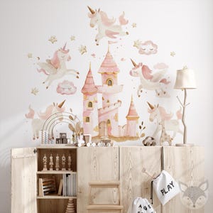 May include: Pink and gold unicorn wall decals with a pink castle and clouds. The decals are on a white wall above a wooden cabinet with shelves.