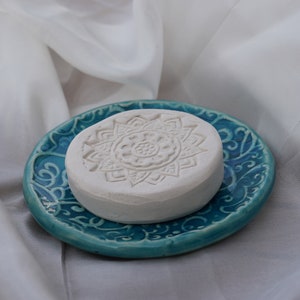 Könnte beinhalten: Eine weiße Keramik-Seifenschale mit einem Mandala-Design auf einer tealblauen Keramik-Schale mit einem floralen Muster.