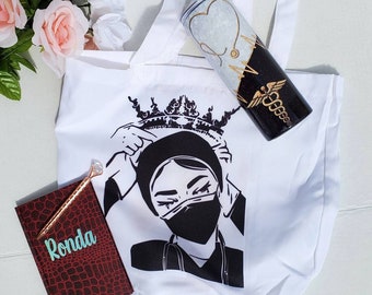 May include: White tote bag with a black and white illustration of a woman wearing a crown and a face mask. The tote bag also includes a black and gold tumbler with a medical symbol and a heart beat graphic. The tote bag also includes a red notebook with the word "Ronda" written on it.