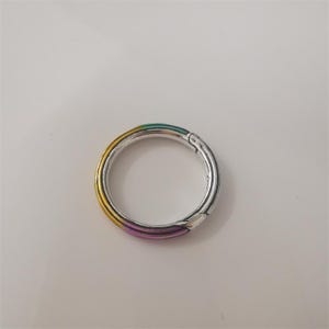 May include: A silver-coloured, circular clasp with a rainbow gradient of colours. The clasp has a hinged opening and a smooth, metallic finish. The colours transition from yellow to green to purple.