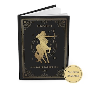 May include: Black journal with a gold foil design featuring the Sagittarius zodiac sign and the name "Elizabeth". The journal has a black cover with gold foil accents and a gold foil Sagittarius zodiac sign.