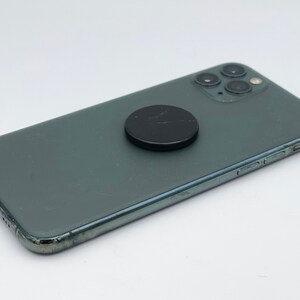 May include: A dark green smartphone with a black magnetic phone ring attached to the back.