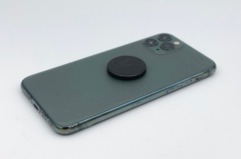 May include: A dark green smartphone with a black magnetic phone ring attached to the back.