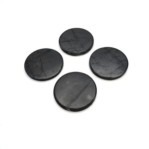 May include: Four round, dark gray coasters with subtle veining. The coasters are made of a stone-like material and are arranged in a square formation against a white background. They appear to be approximately 4 inches in diameter.