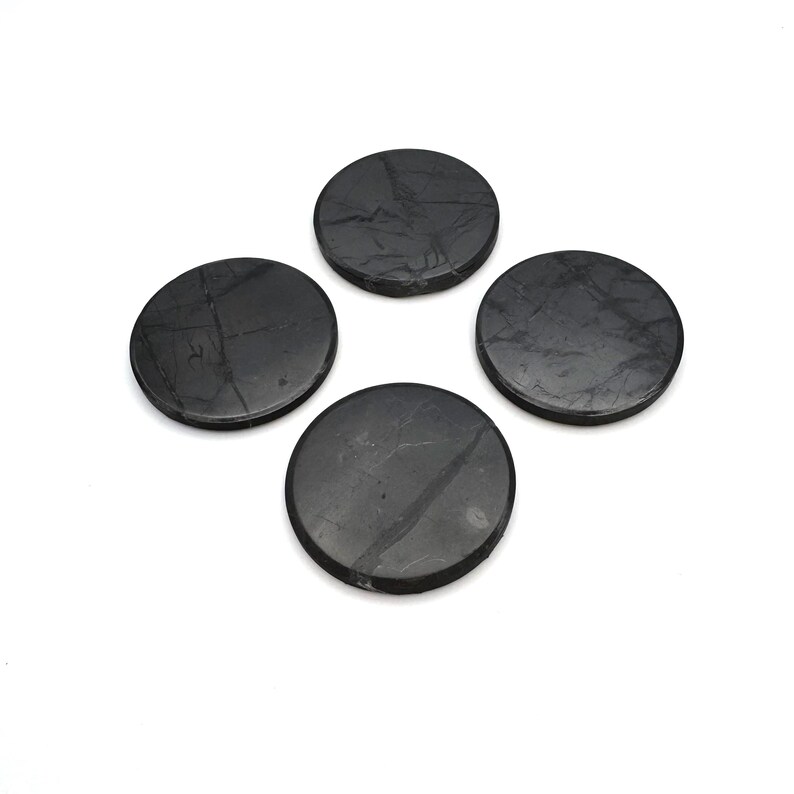 May include: Four round, dark gray coasters with subtle veining. The coasters are made of a stone-like material and are arranged in a square formation against a white background. They appear to be approximately 4 inches in diameter.