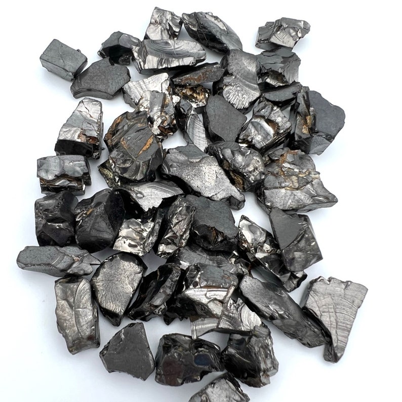 May include: A pile of black obsidian rough stones. The stones are irregularly shaped and have a shiny, almost metallic, appearance.