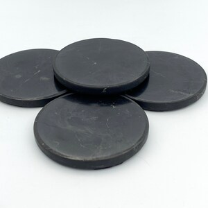 May include: Four black, round coasters with a subtle marbled pattern. These coasters are made of a solid material and are designed to protect surfaces from drink condensation. The coasters are arranged in a slightly overlapping pattern.