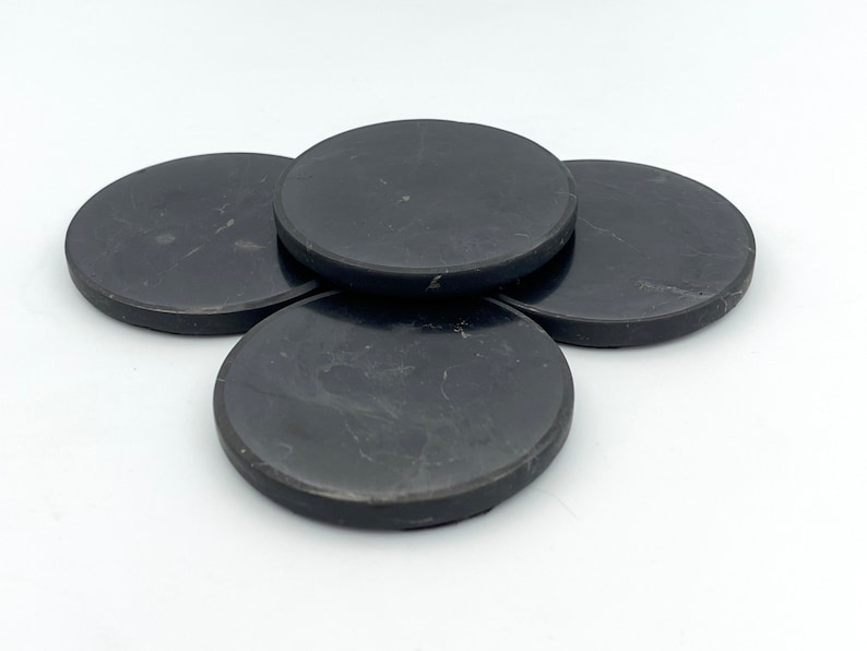 May include: Four black, round coasters with a subtle marbled pattern. These coasters are made of a solid material and are designed to protect surfaces from drink condensation. The coasters are arranged in a slightly overlapping pattern.