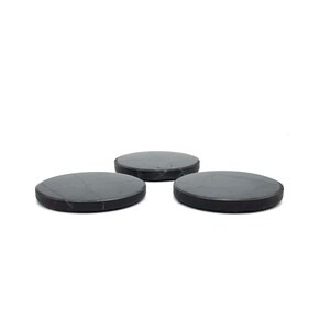 May include: Three round, dark gray coasters with a subtle marbled pattern. The coasters are made of a solid material and have a smooth surface. They are arranged in a triangular formation against a white background.