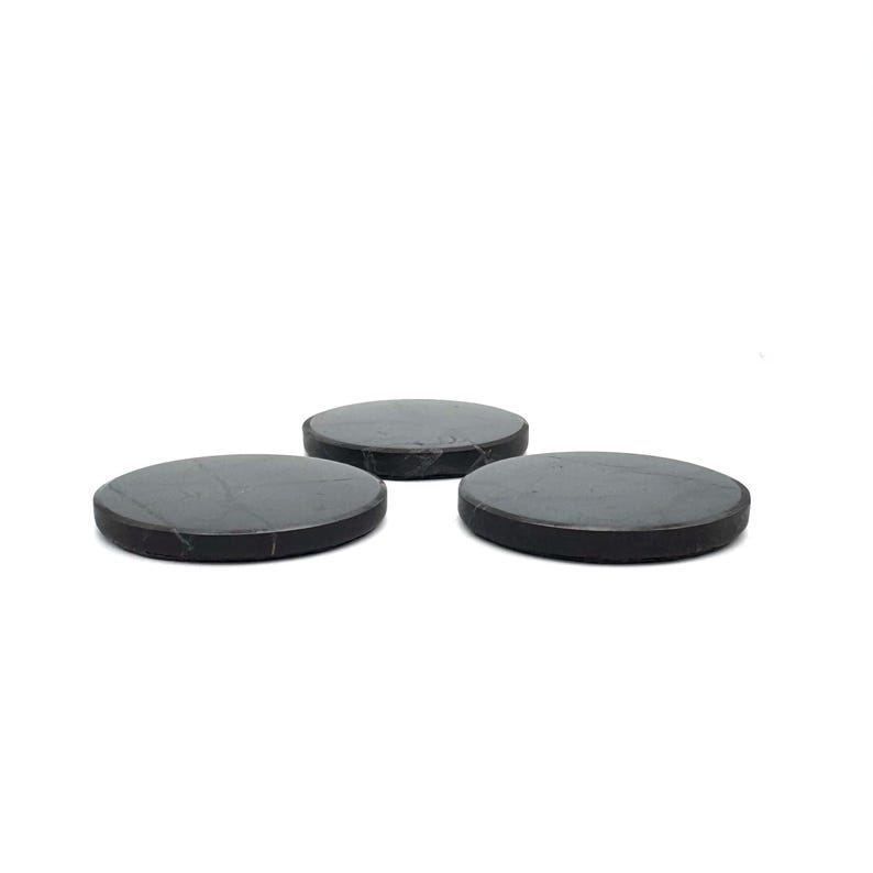 May include: Three round, dark gray coasters with a subtle marbled pattern. The coasters are made of a solid material and have a smooth surface. They are arranged in a triangular formation against a white background.