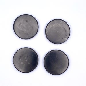 May include: Four round coasters with a dark gray, marbled appearance and a black border. The coasters are arranged in a square formation against a white background. These coasters are designed to protect surfaces from drink rings.