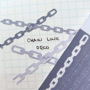 Puede incluir: Primer plano de recortes de papel de eslabones de cadena de color púrpura claro dispuestos sobre papel cuadriculado. Las palabras "CHAIN LINK DECO" están escritas a mano con tinta negra. Vista parcial de una hoja con contornos de eslabones de cadena.