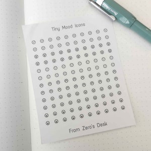 Puede incluir: Una hoja de papel blanco con una cuadrícula de pegatinas de caras sonrientes en blanco y negro. La hoja está titulada "Tiny Mood Icons" y tiene el texto "From Zero's Desk" en la parte inferior.