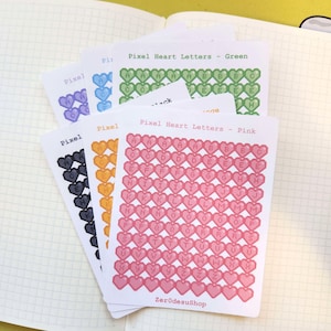 Peut inclure: Quatre feuilles d'autocollants avec des lettres en forme de cœur pixelisées dans différentes couleurs. Les lettres sont en ordre alphabétique. Les couleurs sont rose, vert, bleu et jaune. Les feuilles sont étiquetées "Pixel Heart Letters - Green", "Pixel Heart Letters - Pink", et "ZerodesuShop".
