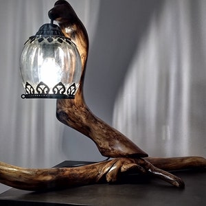 Puede incluir: Una base de lámpara de madera con forma de rama con una pantalla de lámpara de vidrio transparente con un marco de metal negro.