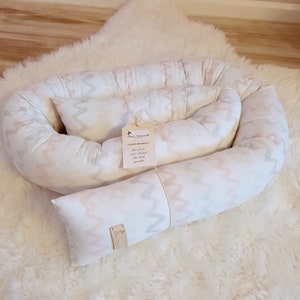 May include: A white and pink patterned baby nest with a tag that reads "My Baby Nest Padded for back support".