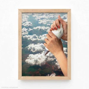 Puede incluir: Una mano sosteniendo una manga pastelera blanca con esmalte de uñas rojo, sobre un fondo de nubes blancas esponjosas y un paisaje verde y marrón.