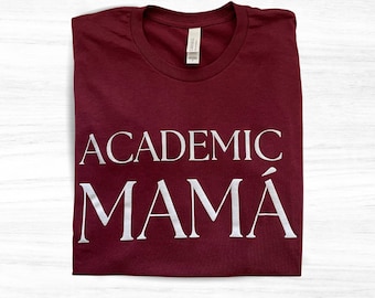 Op de afbeelding: Bordeauxkleurig T-shirt met witte tekst die "Academic Mamá" luidt.