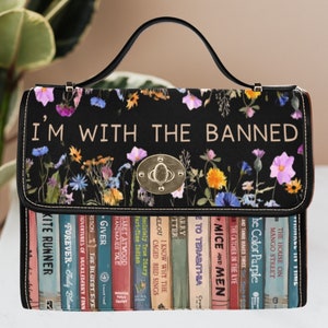 May include: A black handbag with a floral print and the text "I'm with the banned". The front of the bag features a row of colorful book spines with titles like "The Catcher in the Rye" and "Kite Runner".