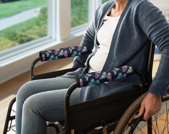May include: Wheelchair armrest covers with a dark blue background and a colorful butterfly pattern. The butterflies are in shades of pink, yellow, blue, and green. The covers are designed to fit over the armrests of a wheelchair.