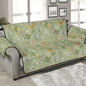 May include: A green quilted sofa cover with a floral pattern featuring a variety of flowers in shades of pink, yellow, and white. The cover has a black trim and is designed to protect furniture from spills and stains.