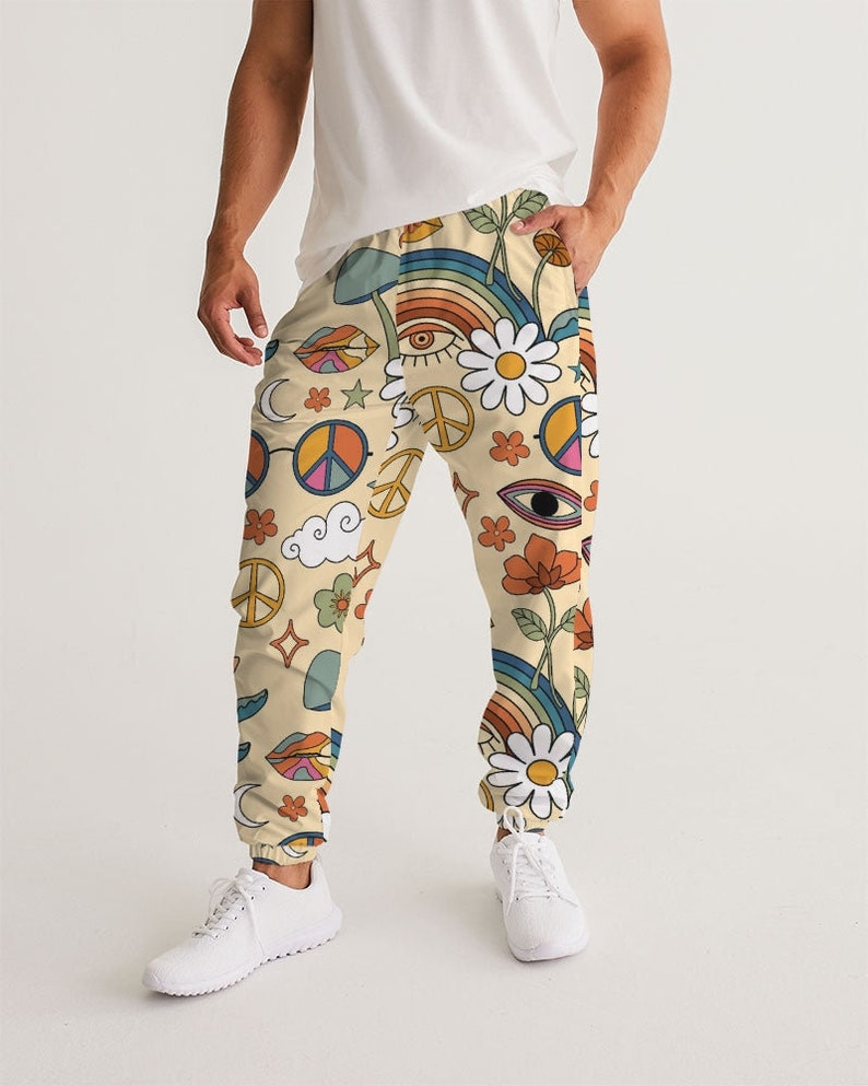 Puede incluir: Un pantal&oacute;n de ch&aacute;ndal de color crema con un estampado retro colorido que incluye s&iacute;mbolos de paz, arco&iacute;ris, flores y ojos.