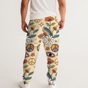Puede incluir: Un pantal&oacute;n de ch&aacute;ndal de color crema con un estampado colorido de signos de paz, flores, arco&iacute;ris y ojos.
