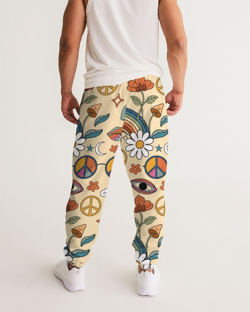 Puede incluir: Un pantal&oacute;n de ch&aacute;ndal de color crema con un estampado colorido de signos de paz, flores, arco&iacute;ris y ojos.