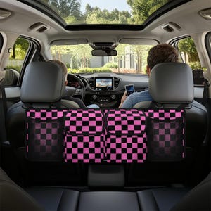 Op de afbeelding: Zwarte en roze geruite autostoel organizer met meerdere vakken. De organizer hangt aan de hoofdsteunen van de achterstoelen van een auto.