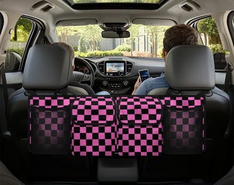 May include: Black and pink checkered car seat back organizer with multiple pockets. The organizer is hanging from the headrests of the back seats of a car.