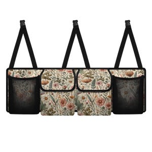 May include: A beige car organizer with three compartments and two mesh pockets. The organizer has a floral print with pink, white, and green flowers. It has black straps for hanging.