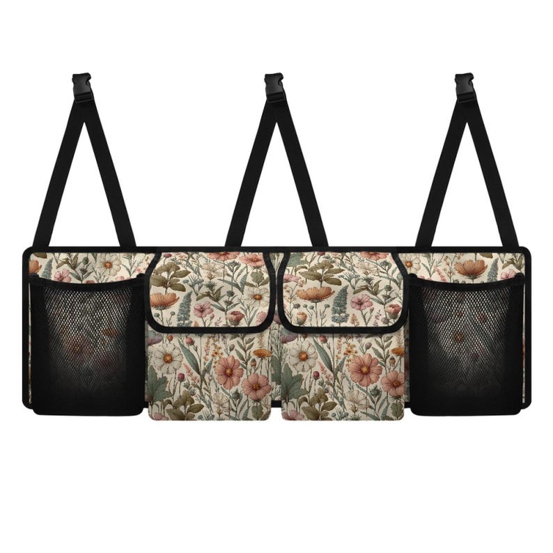 May include: A beige car organizer with three compartments and two mesh pockets. The organizer has a floral print with pink, white, and green flowers. It has black straps for hanging.