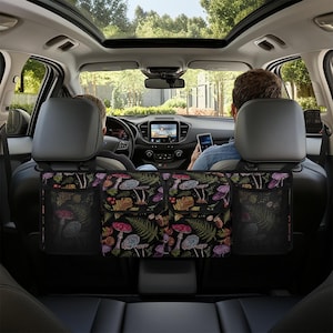 May include: A black car seat organizer with a colorful mushroom and fern pattern. The organizer has two mesh pockets and two larger compartments. The car interior is visible, with two people in the front seats.