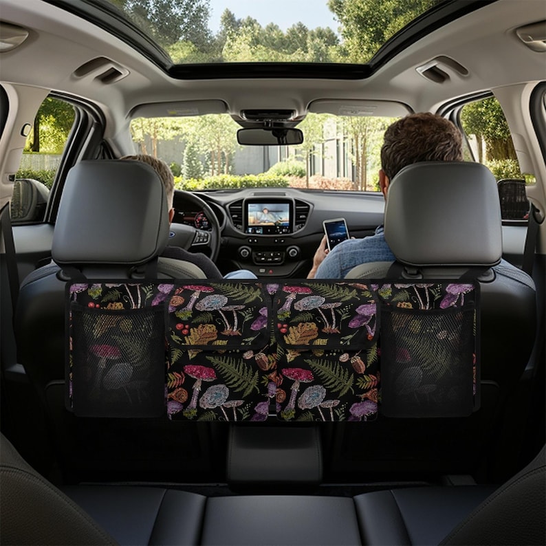May include: A black car seat organizer with a colorful mushroom and fern pattern. The organizer has two mesh pockets and two larger compartments. The car interior is visible, with two people in the front seats.