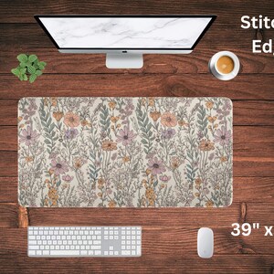 May include: A floral patterned desk mat with stitched edges. The mat is 39 inches by 20 inches and features a light beige background with a variety of pink, yellow, and green flowers.