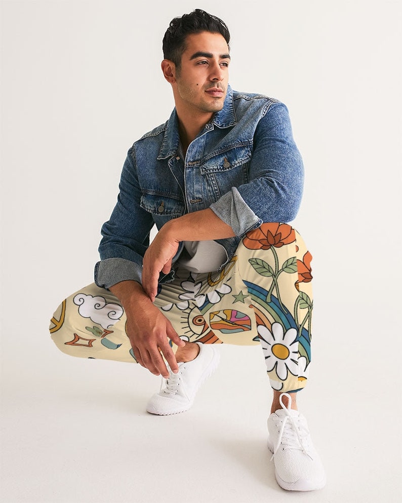Puede incluir: Una persona que lleva una chaqueta vaquera y pantalones de color crema con un estampado colorido de flores, arco&iacute;ris, estrellas y nubes.