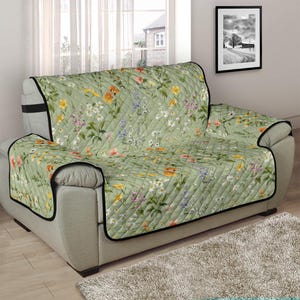 May include: A green floral sofa slipcover with a quilted pattern. The slipcover features a variety of flowers and leaves in shades of pink, yellow, and white.
