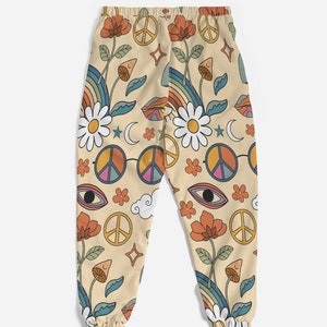 Puede incluir: Pantalones de ch&aacute;ndal beige con un estampado retro de los a&ntilde;os 70 con signos de paz, flores, arco&iacute;ris y ojos.