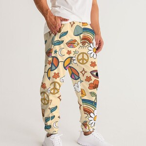 Puede incluir: Un pantal&oacute;n de ch&aacute;ndal de color crema con un estampado colorido de signos de paz, arco&iacute;ris, ojos, flores y setas.