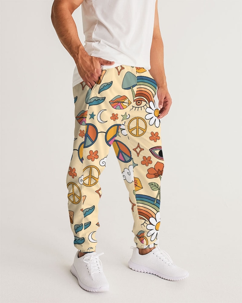 Puede incluir: Un pantal&oacute;n de ch&aacute;ndal de color crema con un estampado colorido de signos de paz, arco&iacute;ris, ojos, flores y setas.