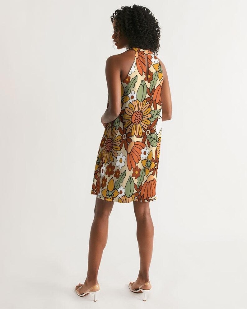 May include: A halter dress with a retro floral print in shades of orange, brown, green, and white on a cream background.