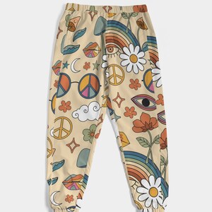Puede incluir: Un pantal&oacute;n de ch&aacute;ndal beige con un estampado retro colorido que presenta signos de paz, arco&iacute;ris, ojos, flores y nubes.