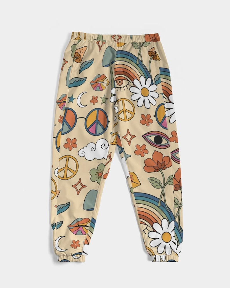 Puede incluir: Un pantal&oacute;n de ch&aacute;ndal beige con un estampado retro colorido que presenta signos de paz, arco&iacute;ris, ojos, flores y nubes.