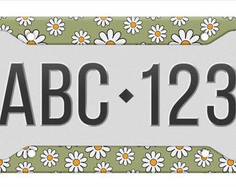 May include: A rectangular license plate frame featuring a sage green background with a repeating pattern of white daisies with yellow centers. The frame has four mounting holes and displays the black text ABC 123 in the center on a light gray field.